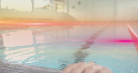 Hand gripping edge of indoor swimming pool with sun glare