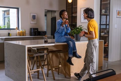 African american woman and asian man chatting over coffee at modern kitchen island