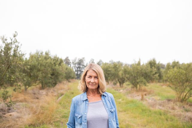 Middle-aged woman smiling while standing in an olive farm. Ideal for use in agricultural promotions, lifestyle blogs, rural living articles, and nature-related content.