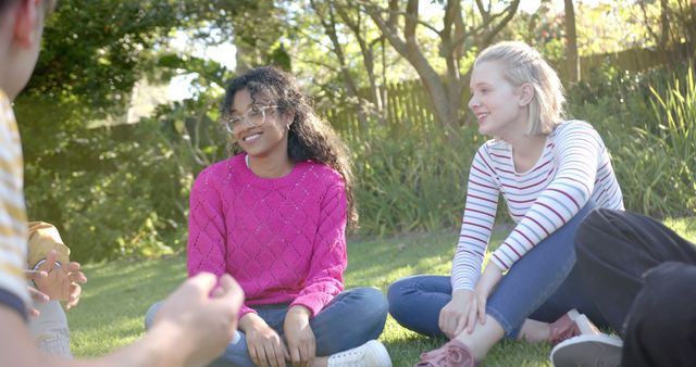 Group of friends hanging out and smiling in sunny park. Trees and greenery visible in background. Ideal for social media campaigns, friendship concepts, outdoor activities, leisure time, youth lifestyle.