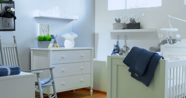 Cosy infant bedroom featuring light gray and white colors. Image includes a white crib with a blanket, a rocking chair, a chest of drawers, and shelves with stuffed animals. Ideal for use in topics related to interior design, home decor, nursery organization, and parenting.