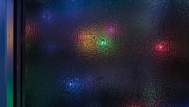 Wet textured glass panel with colorful bokeh reflections and water droplet distortion