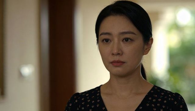Thoughtful asian woman in home doorway wearing dark floral blouse, soft interior light