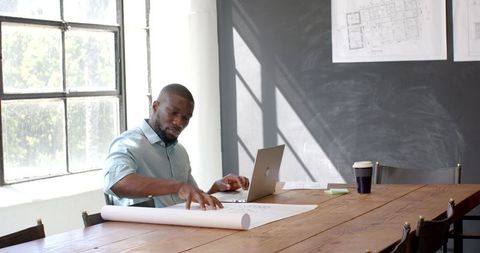 Architect Designing Blueprints on Laptop in Modern Office