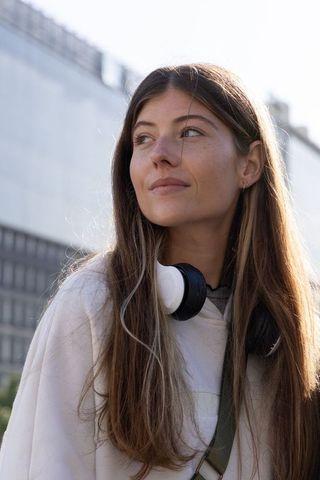 Sunlit city portrait of young woman wearing hoodie and headphones, looking thoughtful