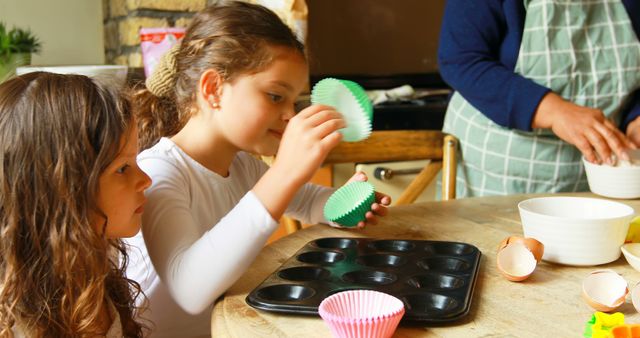 Two young children are preparing to bake cupcakes on a wooden table. They are placing cupcake liners into a baking tray under the supervision of an adult. This scene captures a fun and educational family bonding activity, suitable for blogs about family time, recipes, parenting, or educational activities for children.