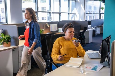 Diverse coworkers collaborating in open-plan office, woman speaking on phone while colleague walks b