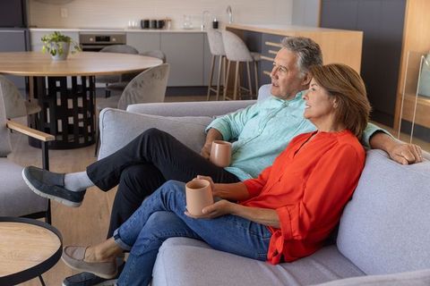 Mature couple relaxing on modern sofa holding coffee in cozy open-plan living room