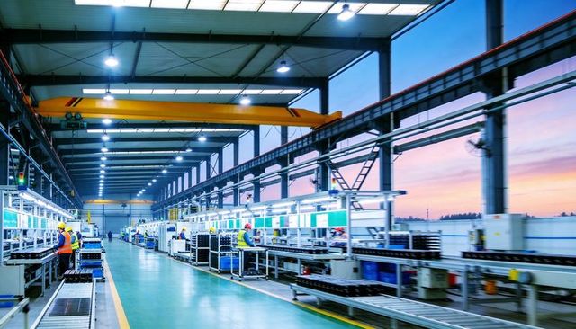Modern factory assembly line with workers operating conveyors and yellow overhead crane