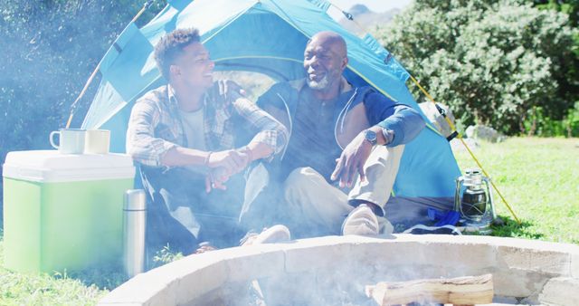 Happy african american father and adult son sitting outside talking by campfire - Download Free Stock Photos Pikwizard.com