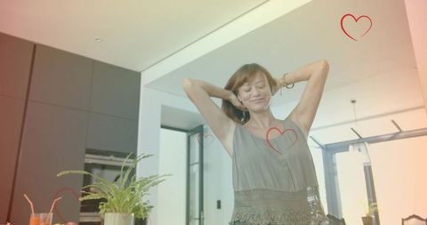 Smiling woman stretching in modern open-plan kitchen with heart overlays, bright lifestyle