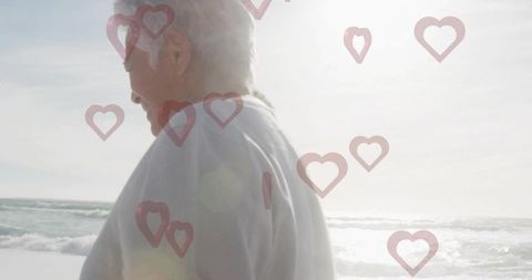 Senior Couple Gazing Toward Sun on Ocean Beach Backlit by Sunlight with Hearts Overlay