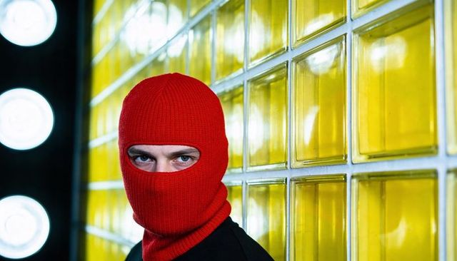 Man wearing red balaclava against yellow glass blocks dramatic studio portrait