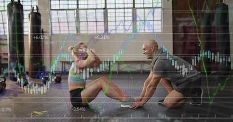 Woman Doing Sit-ups While Trainer Holding Feet in Industrial Gym With Kettlebells