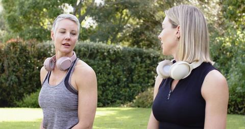 Women chatting after outdoor workout wearing wireless over-ear headphones in park