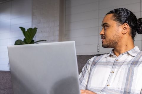 Asian man working on laptop from sofa in modern minimal living room