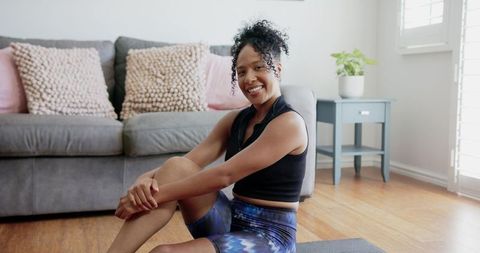 African american woman stretching at home smiling after workout in bright living room
