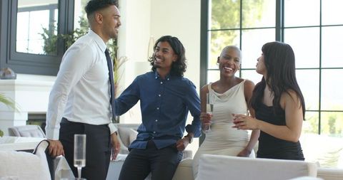 Diverse friends laughing and toasting champagne in modern sunlit lounge for celebration