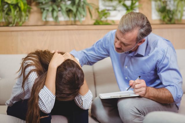 Therapist providing emotional support to a distressed female patient in an office setting. Ideal for use in articles or websites about mental health, therapy, counseling services, emotional support, and professional healthcare.