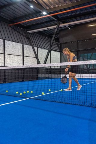 Female athlete training on indoor blue court with paddle racket and scattered tennis balls