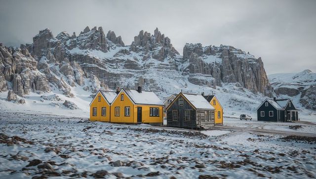 Yellow cabins nestling on snowy plain with dramatic rocky mountain backdrop
