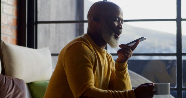 African American man using a smartphone at home, with copy space. He's comfortably seated, engaging in a voice conversation.