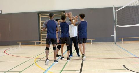 Volleyball team high-fiving and huddling at center court in indoor gymnasium