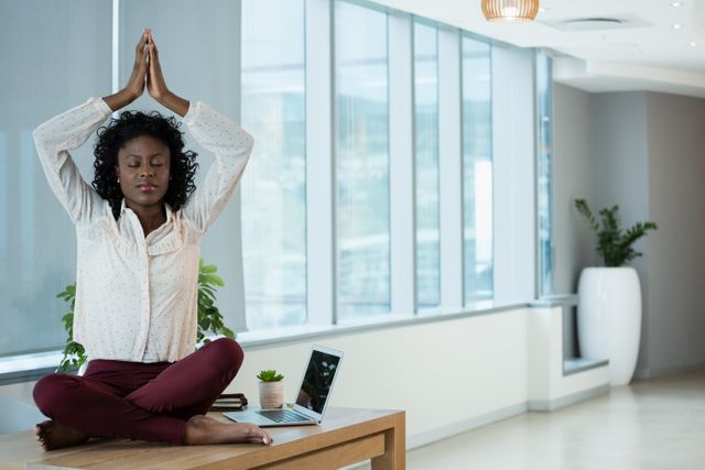 Image shows a businesswoman practicing mindfulness and relaxation techniques by meditating on her desk in an office setting. This visual is ideal for promoting workplace wellness, mental health awareness, and stress relief strategies. It can be used in blogs, presentations, or articles about balancing work and personal well-being.