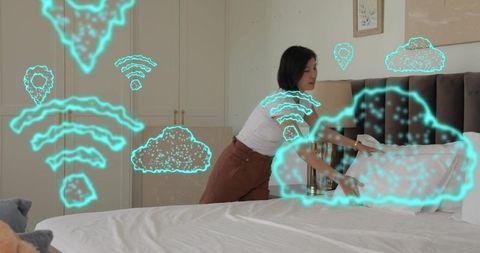 Korean woman making bed in modern bedroom with holographic smart home icons