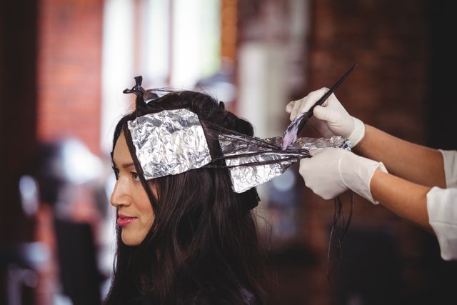 Hairdresser applying hair dye to client's hair using foils in a professional salon. Ideal for use in beauty and hair care advertisements, salon promotions, hairstyling tutorials, and articles about hair treatments and beauty services.