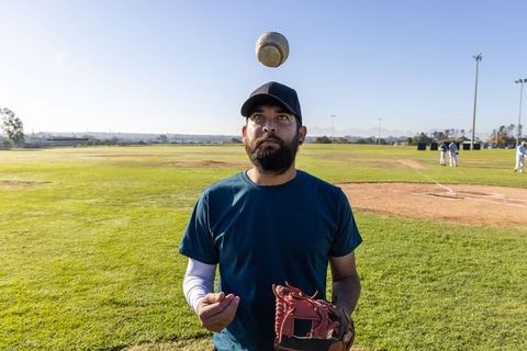 Baseball player practicing catch on sunny outfield with glove, cap and focused expression