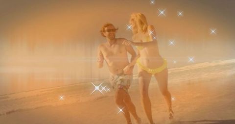 Couple running and laughing on sunlit beach at sunset wearing yellow bikini and floral trunks