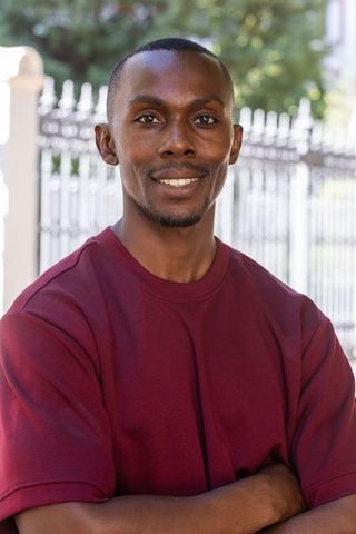 African american man smiling and standing with arms crossed in residential yard by iron fence