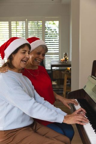 Senior Friends Wearing Santa Hats Playing Piano During Holiday Season