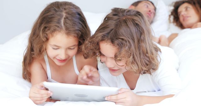 Siblings Watching Tablet in Bed with Parents Resting in Background - Download Free Stock Images Pikwizard.com