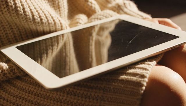 Sunlit white tablet resting on chunky beige knit lap reflecting glossy scratched screen