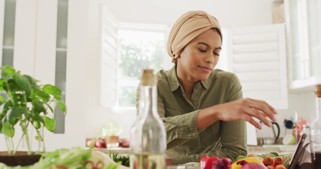Image of happy biracial woman in hijab using smartphone in kitchen. Lifestyle, cooking, spending free time at home concept.