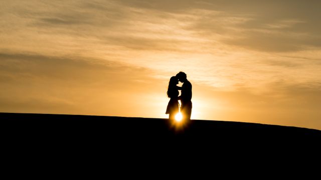 Couple sharing an intimate moment at sunset on a hilltop, producing a silhouettes against the warm evening sky. Ideal for use in romantic themes, relationship advice, greeting cards or travel promotions highlighting romantic getaways.