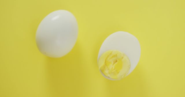 Hard-boiled egg shown alongside halved egg displaying yolk and egg white against yellow background. Useful for food blogs, nutrition articles, healthy eating promotions, cookbooks, and menus.