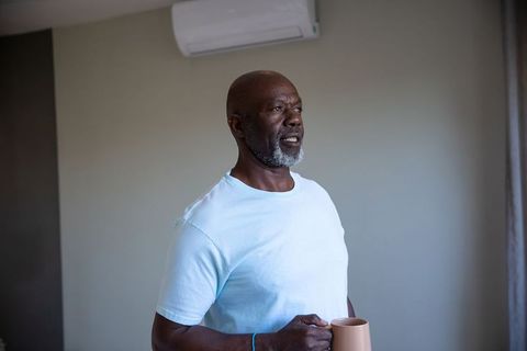 Senior man relaxing with coffee at home near air conditioner