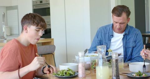 Father and teen eating salad at modern kitchen table during casual family meal