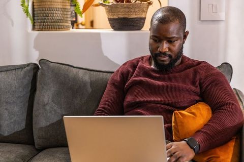 African american man working on laptop on couch in cozy living room home office