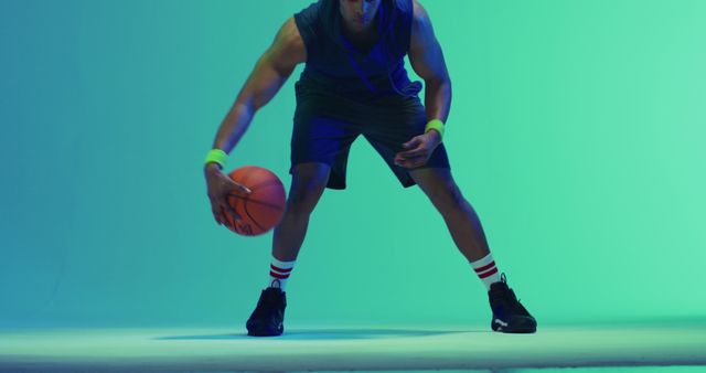 Image of biracial male basketball player bouncing ball on green to blue background. Sports and competition concept.