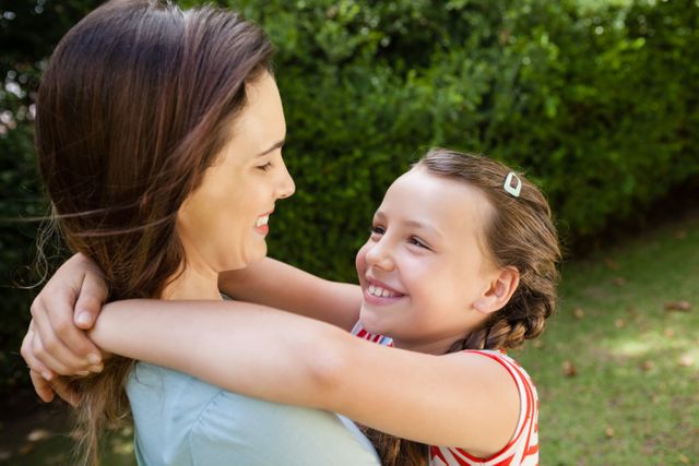 This image captures a joyful moment between a mother and her daughter as they embrace in a backyard. Ideal for use in family-oriented advertisements, parenting blogs, and social media posts celebrating family bonds and outdoor activities.