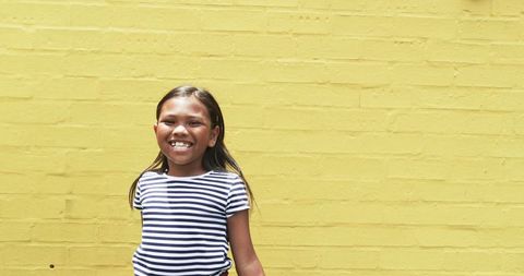 Smiling Young Girl Against Yellow Brick Wall with Space for Text