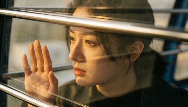 Young woman pressing palm to train window, gazing through golden-hour bars and glass