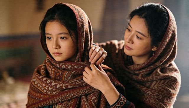 Mother adjusting daughter's patterned woven shawl, tender care ritual in warm interior