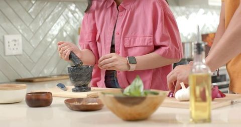 Asian couple cooking together using mortar and pestle on kitchen island chopping garlic