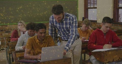 Teacher leaning over helping student using laptop in classroom for collaborative learning