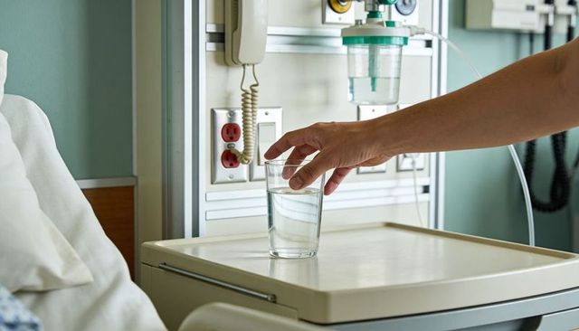 Adult hand reaching for glass of water on hospital overbed tray next to medical panel